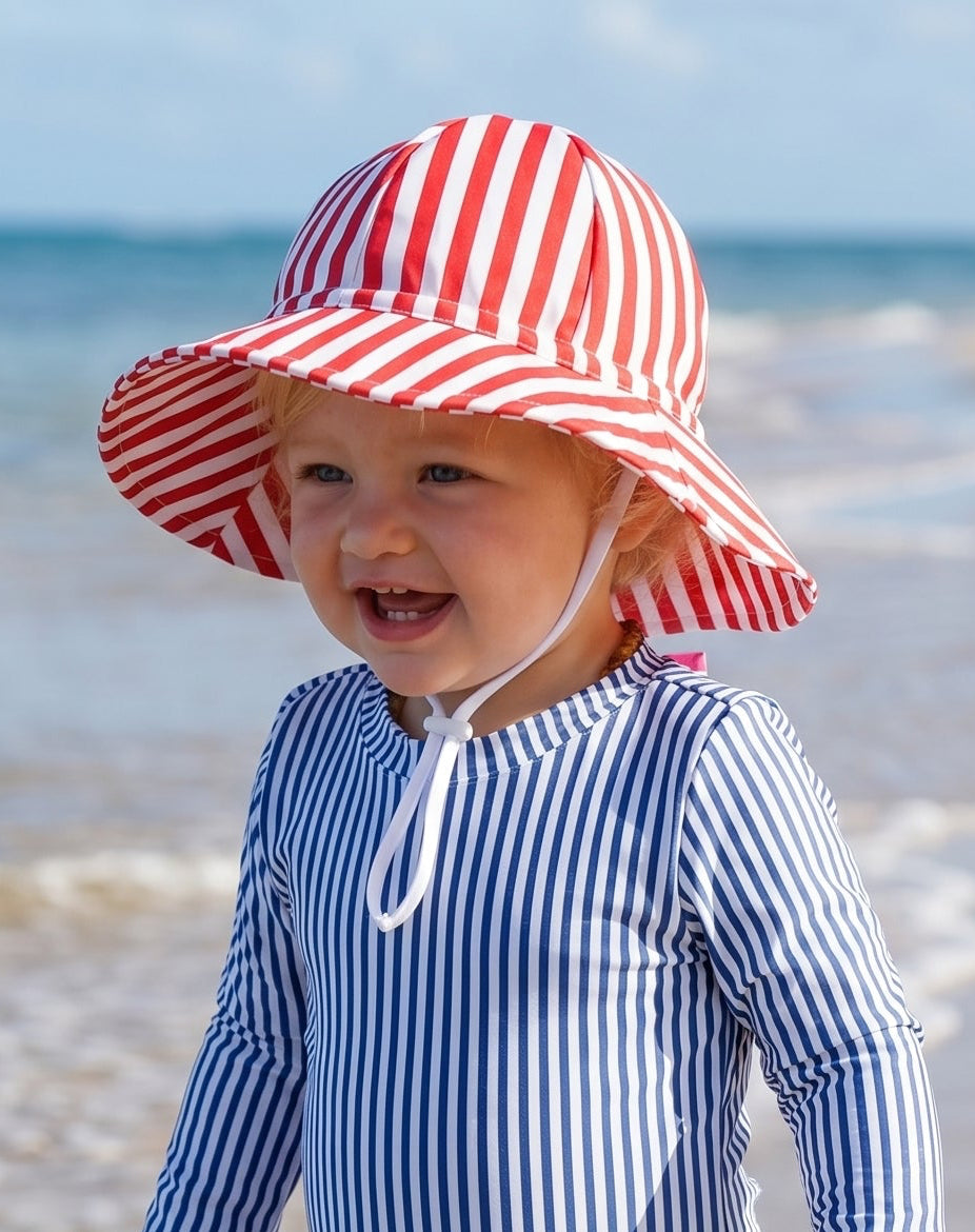 Child in a striped swimsuit and sun hat playing on a beach